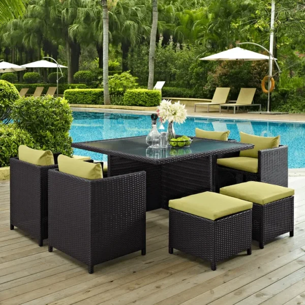 7-piece dark brown wicker outdoor dining set with green cushions, including ottoman and table without glass top