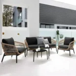 Outdoor garden 4 seater rope sofa in beige cushions and black frame placed on a patio with greenery.