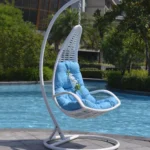 White single-seater hanging swing with a sturdy stand, placed in a garden setting.