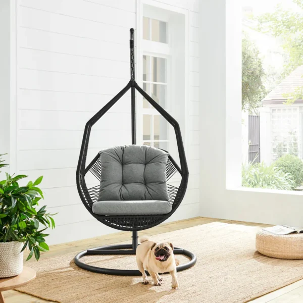 Single-seater hanging swing with a black braided rope and metal stand, placed in a garden setting.