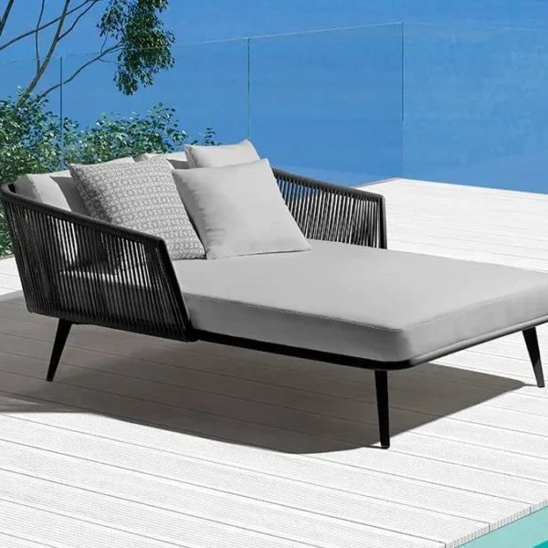 Black and grey patio rope daybed set with cushions placed outdoors on a wooden deck surrounded by greenery.