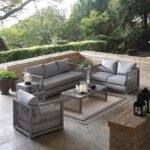 Outdoor 6-piece rattan wicker sectional sofa set in silver and grey, placed in a garden setting with cushions.