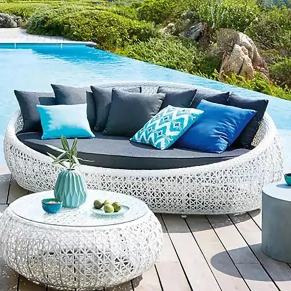 White outdoor rattan wicker daybed set with cushions and matching glass-top table for patio and garden spaces.