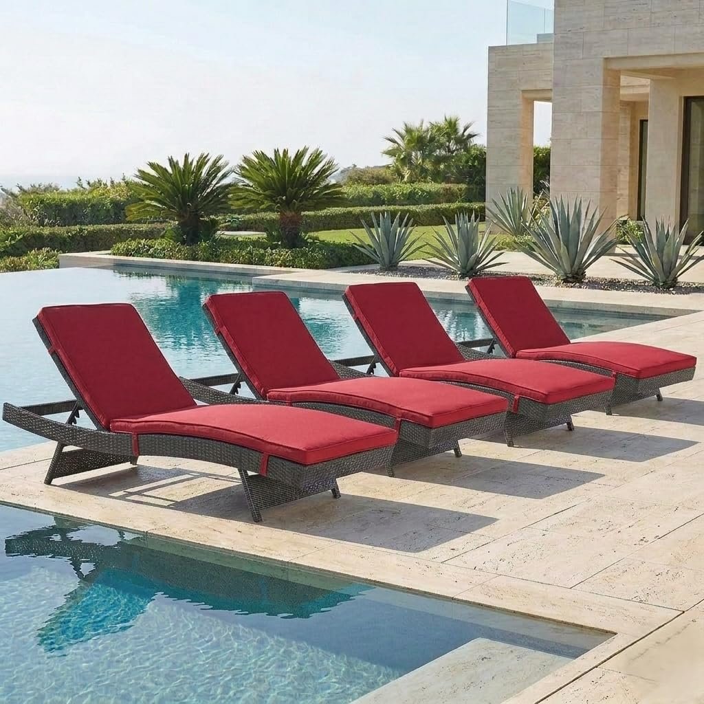 Four red cushioned wicker lounge chairs arranged poolside on stone patio with landscaped garden and palm trees.