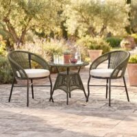 Loccus 2 Seater Outdoor Patio Furniture Set with two handwoven rope chairs, cream cushions and round glass-top table in a garden setting.